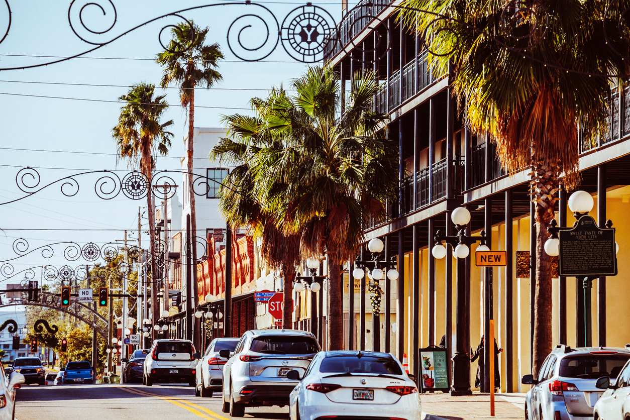 Street scene with cars, palm trees, and decorative archways in a sunny urban setting.