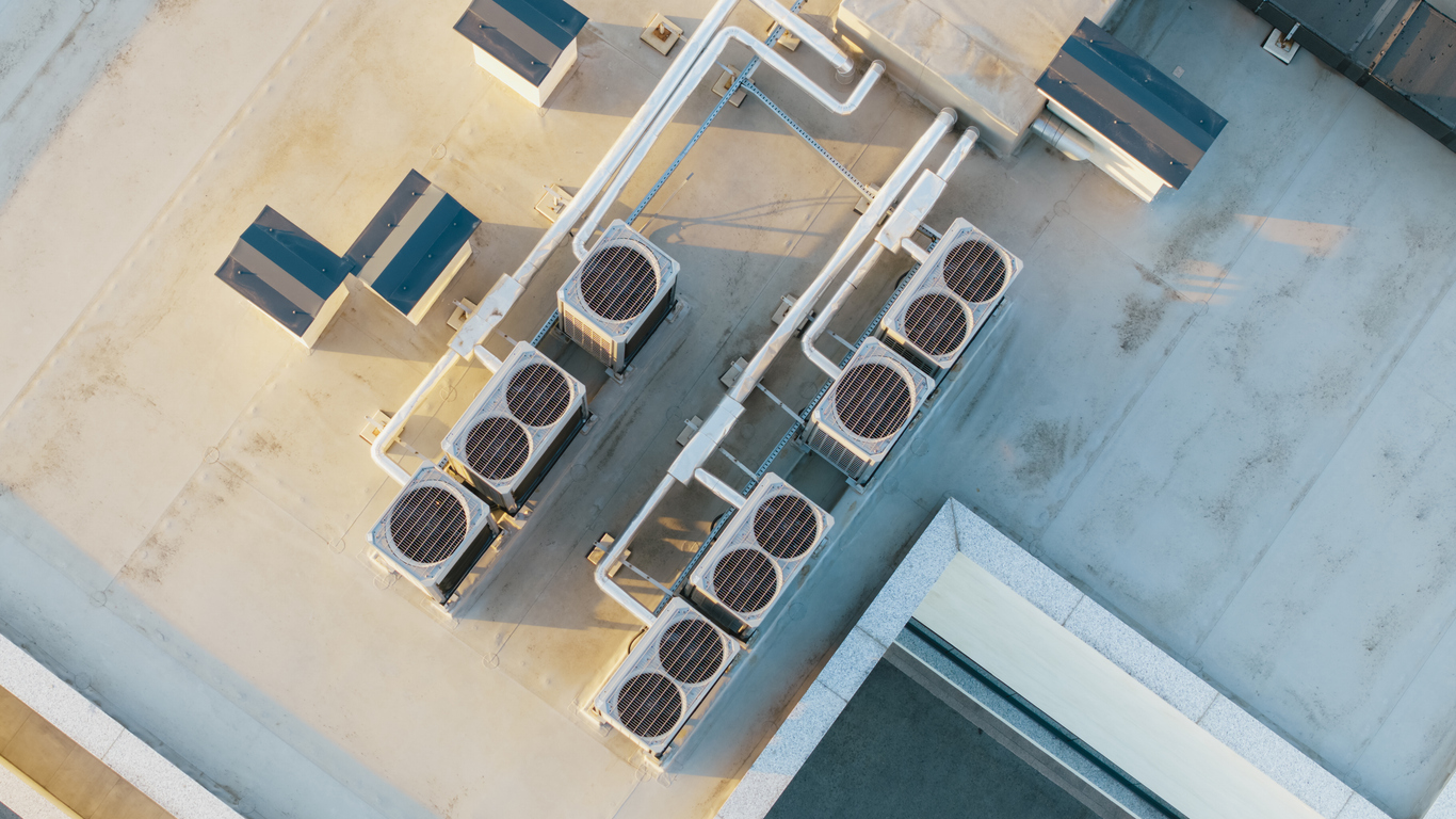 Aerial view of industrial rooftop HVAC units with pipes and ductwork in a geometric arrangement.